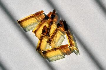 Ampoules with a beauty drug on a gray background with stripes of shadows.