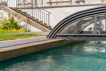 Fototapeta premium Vue d’une piscine couverte entourée d’un caillebotis en bois, intégrée harmonieusement dans un jardin paysager conçu par une entreprise spécialisée.