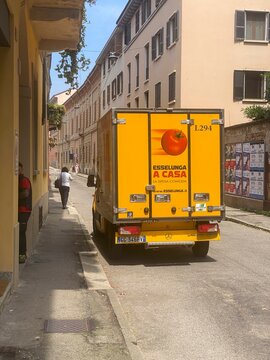 Yellow Mercedes Benz Sprinter delivering groceries for Esselunga a Casa, parked on narrow Italian street, driver standing nearby, pedestrian walking past