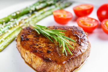 Close up, macro of tasty grilled beef steak served with green asparagus and cherry tomatoes on white plate, with cutlery. Perfect for food menu, diet, or culinary design concepts.