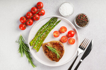 Tasty grilled beef steak served with green asparagus and cherry tomatoes on white plate, with cutlery and spices. Perfect for food menu, diet, or culinary design concepts. Top view, flat lay
