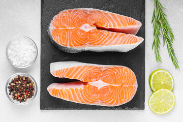 Two fresh raw salmon or trout steaks on white stone surface with food ingredients. Tomatoes, lime,...