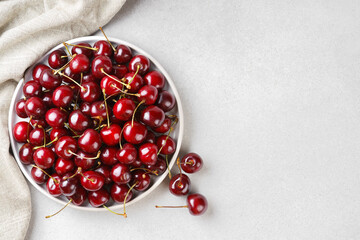 Close up of white plate filled with ripe red sweet cherry placed on light linen napkin on white background. Delicious food, juicy summer fruit, healthy eating. Top view, copy space