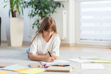Girl drawing on floor surrounded by notebooks.