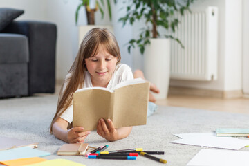 Smiling preteen girl reading book on carpet