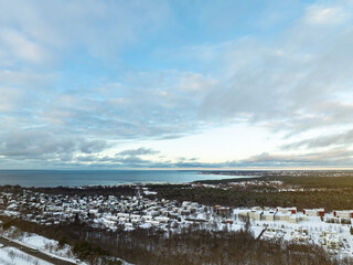 Aerial winter view of Pirita district in Tallinn, Estonia. Snow-covered houses, pine forests, and the Baltic Sea under a dramatic sky create a peaceful, scenic Nordic coastal landscape