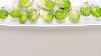 Raw organic Brussel sprouts on white plate on grey background, top view. Flat lay, overhead, from above. Copy space.