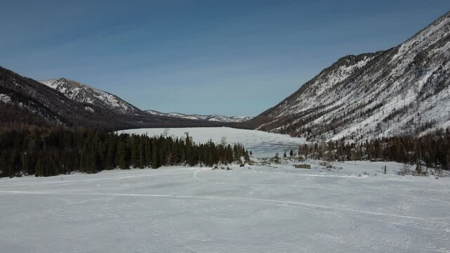 Drone aerial footage of a snowmobile riding across a frozen lake and snowy terrain in Russia. Captured from various angles, this footage highlights winter adventure, remote wilderness