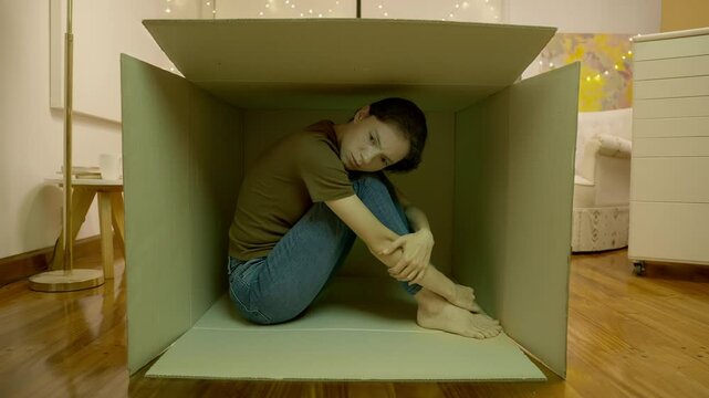 Young teenage girl sitting in a cardboard box closed off from the outside world. Depression and loneliness