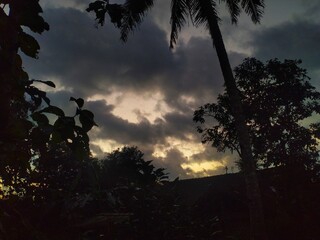 A dramatic sunset or sunrise sky with dark, heavy clouds and a sliver of golden light on the...