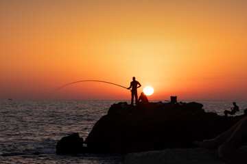 fishermen fishing in the evening by the sea on the Mediterranean sea coast of Caesarea in Israel at sunset time in the direction of the setting sun. High quality photo