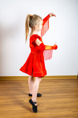 charming 5-year-old blonde girl, dancer in vibrant red dress performs Latin dance steps, showing...