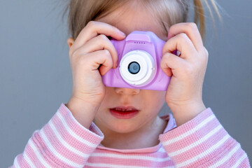 Preschool girl plays with toy camera, pink striped shirt, learning photography, early creativity,...