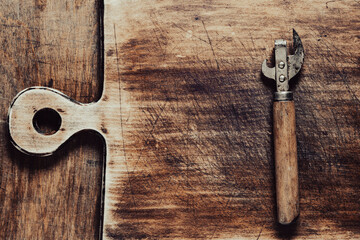 Old rusty bottle opener and canned food on a wooden cutting board background, top view, closeup,...