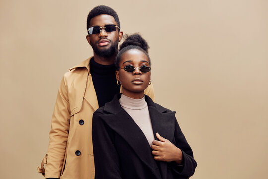 Stylish couple wearing sunglasses, posing confidently against a warm beige background, showcasing modern fashion and urban elegance in a seasonal autumn setting - Powered by Adobe