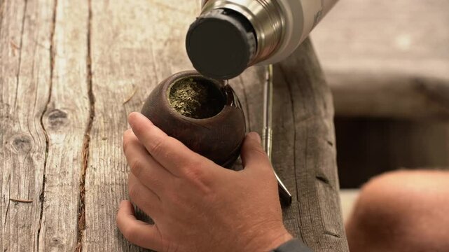 Man preparing traditional yerba mate infusion on rustic wooden surface