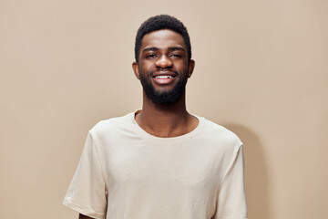 Smiling Black man in a casual beige t shirt, showcasing joy against a neutral background,...
