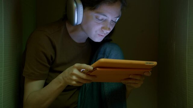 Teen playing game on tablet sitting inside cardboard box, deprived of adult attention. Cardboard box as symbol of her world