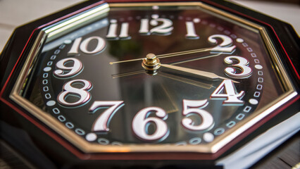 Octagon clock face with white numbers and gold hands showing time with decagon shape frame and reflective glass surface