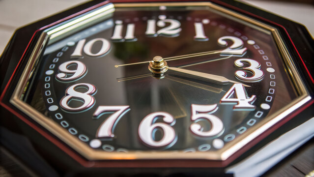 Octagon clock face with white numbers and gold hands showing time with decagon shape frame and reflective glass surface
