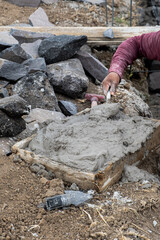 Hands of a Mexican bricklayer scooping cement mortar with a metal spoon at work