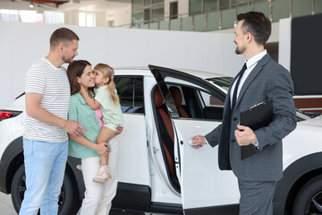Salesman with clipboard showing new car to happy family in salon