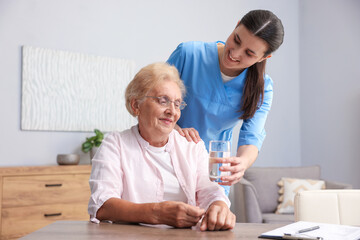 Nurse giving glass of water to senior woman indoors. Home health care service