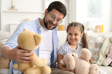 Father and his daughter playing with teddy bears on sofa at home