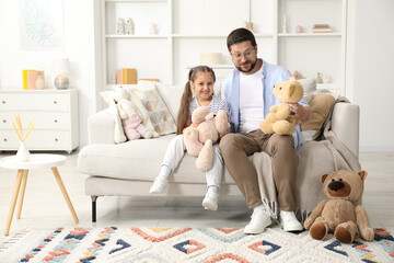 Father and his daughter playing with teddy bears on sofa at home