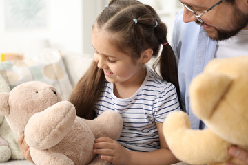 Father and his daughter playing with teddy bears on sofa at home, closeup