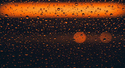 Rain drops on a window with orange light reflecting through the glass in a dark and moody setting
