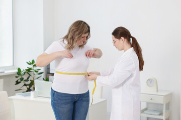 Weight loss. Nutritionist measuring overweight woman's waist with tape in clinic