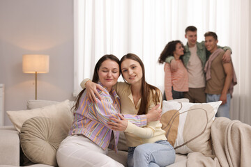 Friends hugging on sofa indoors, selective focus