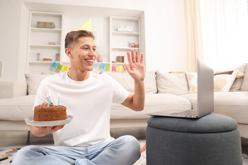 Man with cake celebrating his birthday and having video call via laptop at home