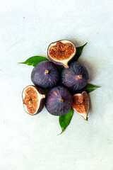 Purple ripe figs fruit and slices with green leaves top view on a stone background