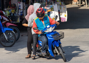 A motorcycle taxi drives a man in a hood and a woman with a hijab