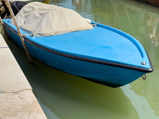 Blue wooden boat with beige cover docked on calm water canal