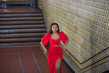 Young, beautiful, African woman, wearing a red dress, posing as a model on the stairs of the square of Spain in Seville. Fashion concept, beauty, trendy.