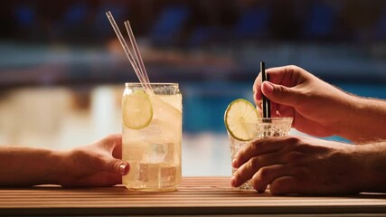 Fruit cocktail in hotel bar, Two cocktail glasses cheers in the hands on sea background. Bartenter making drink in bar, Summer vacation concept, A beautiful couple enjoy the vacation at the beach. - Powered by Adobe
