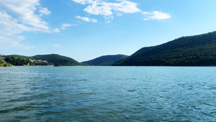 Serene landscape featuring calm blue water reflecting the sky, surrounded by lush green hills under a bright sunny day, creating a peaceful natural environment 