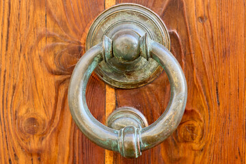 Close-up of an old circular door knocker hanging on a wooden door, showing the texture of the wood and the metal.