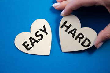 Easy or Hard symbol. Concept word Easy or Hard on wooden hearts. Businessman hand. Beautiful blue...