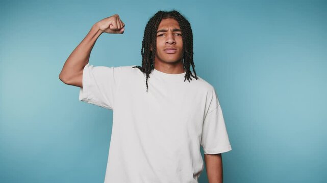 young african american man on a blue background looking at the camera and showing his strength flexing his biceps posing for the camera, wearing a white t-shirt