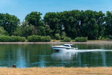 Sunny day on the river highlights a sleek boat gliding through calm waters in a lush riverbank...