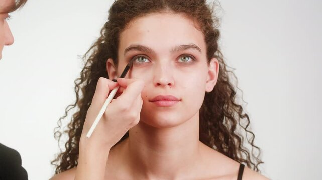 Eye shadow makeup to the upper eyelid, close-up. Makeup artist applies a bright eye shadow with a make-up brush.Tutorial master class of professional makeup, smoky eyes 