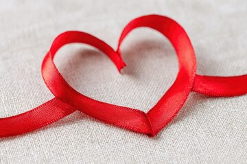 Red ribbon forming heart shape on white fabric background