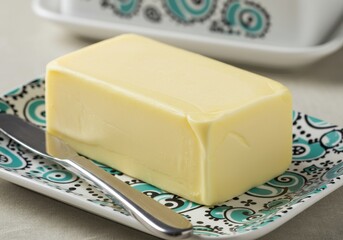 A rectangular block of yellow butter rests on a decorative dish with a knife