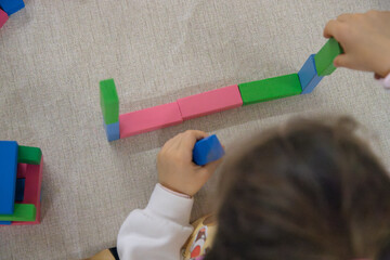 A young child plays indoors during the day, focusing intently while building a structure with colorful wooden blocks, developing fine motor skills, creativity, and early cognitive abilities.