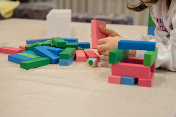 A young child plays indoors during the day, focusing intently while building a structure with colorful wooden blocks, developing fine motor skills, creativity, and early cognitive abilities.