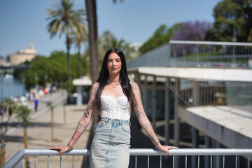 Young woman, brunette, tall, slim and very tattooed, wearing white top and denim skirt, posing...